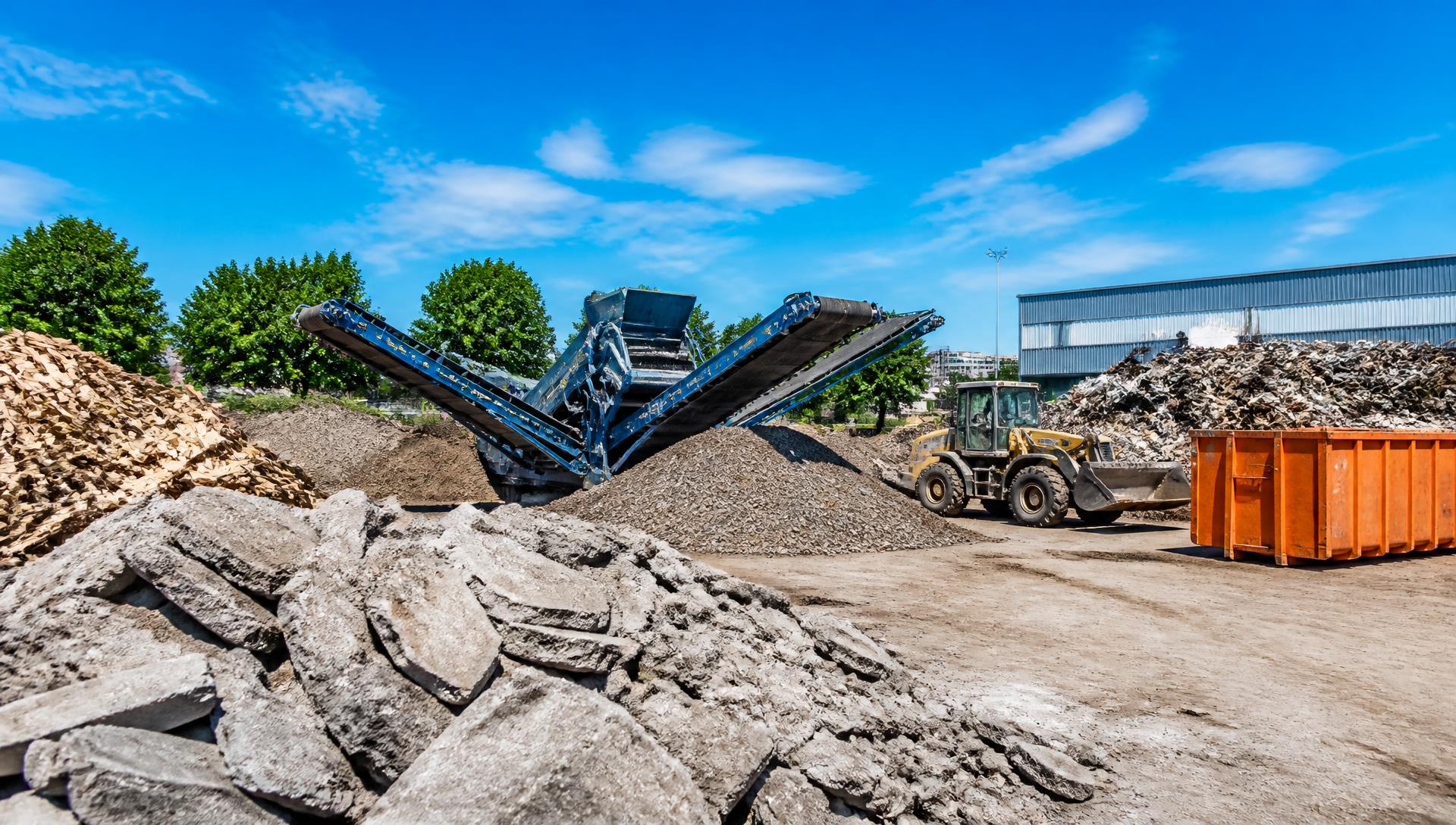 Areál na zpracování odpadu s roztříděnými hromadami materiálu a mobilním drtičem